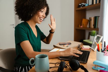 African american young woman with curly afro hairstyle sitting at desk and using laptop at home